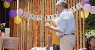 Büyükbaba dışarıda torunuyla oynuyor, çeşitli aileler eğlenceye katılıyor. Nesiller, neşeli, bağlanan, boş zaman, mutluluk