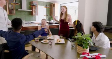 Çeşitli arkadaşlar mutfakta yemek masasında oturmuş mezuniyette konuşma yapmak için alkışlıyorlar ve selfie çekiyorlar. Kutlama, arkadaşlık, çeşitlilik, sosyal, modern, neşe, başarı