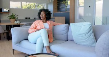 Afro-Amerikalı çift kanepede dinleniyor, evde kahve ve hamur işlerinin tadını çıkarıyorlar. Beraberlik, rahatlık, yaşam tarzı, ev, rahatlık, konfor.