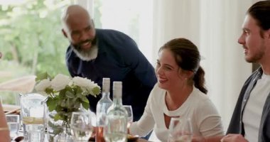 Çeşitli arkadaşlar yemek masasının önünden geçerken şarap kadehleri içip hoparlör dinliyorlar. Kutlama, neşe, bağlantı, sıcaklık, birliktelik, kırsallık, coşku