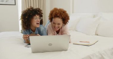 Lezbiyen çift dizüstü bilgisayar ve defter kullanarak yatakta dinleniyor, evde birlikte vakit geçiriyorlar. Yaşam tarzı, rahatlama, teknoloji, samimiyet, ev, eğlence.