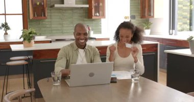 Çeşitli çiftler evde başarıyı kutluyor, kadınlar dizüstü bilgisayar kullanırken tezahürat yapıyor. Kutlama, takım çalışması, mutluluk, teknoloji, iletişim, işbirliği