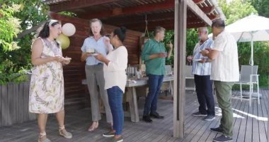 Çeşitli yaşlılar bahçe kutlamalarında eğleniyor, sohbet ediyor ve ahşap güvertede yemek yiyorlar. Yaşlı, kutlama, toplanma, arkadaşlık, bahçede, boş zaman