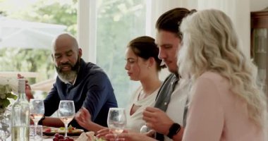 Çeşitli arkadaşlar evde yemek masasında şarap içerken kadeh kaldırırken ve yeni geleni karşılarken el kol hareketi yapıyorlar. Kutlama, dostluk, neşe, zarafet, rahatlık, açık hava, içecek.