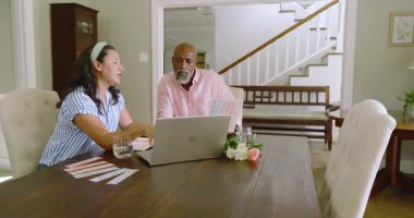 Üst düzey çift evde dizüstü bilgisayar ve evraklarla planları tartışıyor. Emeklilik, finans, planlama, yaşlılık, teknoloji, tartışma