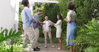 Çeşitli arkadaşlar bahçede kutlama yapıyor, gri tişörtlü adam tablet okuyor ve yüzükle evlenme teklif ediyor. Kutlama, dostluk, romantizm, açık hava, zarafet, mutluluk, nişan