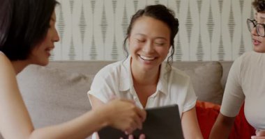 Çeşitli bayan arkadaşlar tablet ve basılı sayfaları paylaşıyor, kanepede tartışıyor, çözümü kutluyorlar. İşbirliği, dostluk, takım çalışması, gündelik, modern, olumlu, iletişim