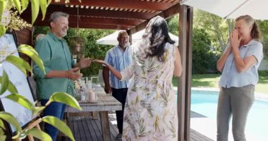 Arka bahçede kutlama yapan çeşitli kıdemli arkadaşlar, neşeli bir buluşmada kucaklaşıp gülümsüyorlar. Kutlama, mutluluk, bağ, birliktelik, şenlik, kucaklama