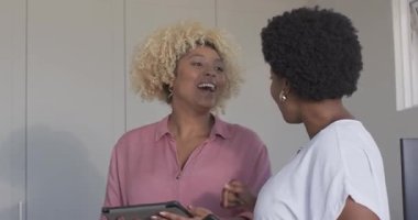 İki kadın birlikte gülüyor, ellerinde tablet ve akıllı telefonla evde sohbetten zevk alıyorlar. Teknoloji, iletişim, arkadaşlık, yaşam tarzı, eğlence, dijital