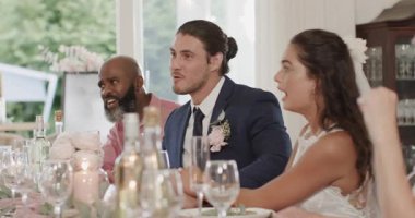 Gelin ve damat baş masada gülümserken erkek misafir konuşma yapıyor, alkışlıyor, mantar patlatıyor. Kutlama, neşe, zarafet, lüks, sosyal, şenlik, konukseverlik