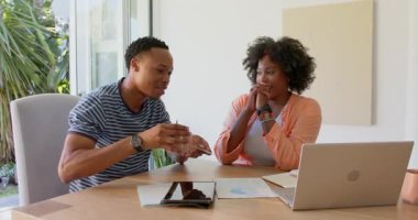 Evdeki genç çift masadaki dizüstü bilgisayar ve tabletle belgeleri tartışıyor. tartışma, teknoloji, evrak, iletişim, takım çalışması, yaşam tarzı