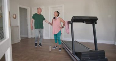 Yaşlı çift evde egzersiz yapıyor, kadın koşu bandında su içiyor. Spor, sağlık, susuzluk, etkinlik, ev içi, rutin