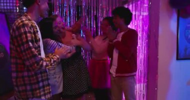 Arkadaşları, Asyalı bir kadının partide saç bandı takmasını sağlayan beyaz bir kadına sarılıyorlar. Kutlama, dostluk, dostluk, canlı, sosyal, şenlikli, gece hayatı.