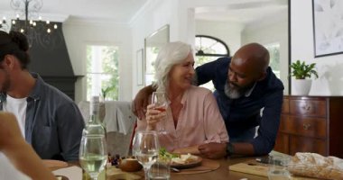 Yetişkin bir Afro-Amerikan erkeği, kutlama günü şarap kadehini kaldırırken son sınıf kadınını kollarıyla sarıyor. Aile, sosyal toplantı, kutlama, sıcak atmosfer, neşeli, kapalı alan, samimi