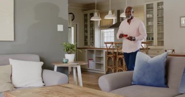 Afro-Amerikalı bir adam kanepede oturup kitap okuyor ve evinde sıcak bir oturma odasında çay içiyor. Rahatlama, rahatlama, rahatlama, hobiler, içecek, ev