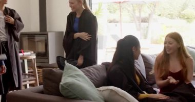 Diploma taşıyor, çeşitli mezuniyet arkadaşları kaynaşıyor, oturma odasında kep ve cübbe ile kutlama yapıyorlar. Kutlama, dostluk, başarı, modern, neşeli, ağ oluşturma, kilometre taşı