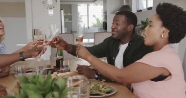 Arkadaşlar birlikte yemek yiyor, gülüyor ve evde yemek masasında alkışlıyorlar. Arkadaşlık, kutlama, mutluluk, toplanma, eğlence, yemek.