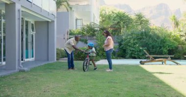 Afrikalı Amerikalı baba oğluna bisiklet sürmeyi öğretiyor, ikisi de gülümsüyor. Aile, ebeveynlik, bağlılık, açık hava, aktivite, çocukluk