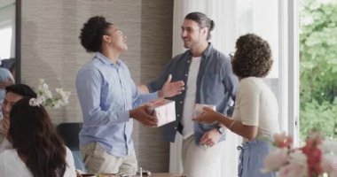 Çeşitli arkadaşlar hediyelerin gelişini kutluyor, hediye kutuları alıyor, yemek masasında sarılıyor ve düzenliyor. Arkadaşlık, kutlama, sosyal toplantı, iç mekan, canlı, neşeli, bağlanma