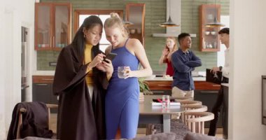 Çeşitli bayan arkadaşlar mutfağa girip telefonlarını paylaşıyor ve içkilerini yudumlarken içeriklerini izliyorlar. Arkadaşlık, sosyalleşme, modern, canlı, yaşam tarzı, etkileşim, toplum