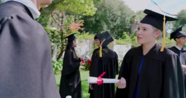 Çeşitli mezunlar çimenlikte kutlama yaparken bir akran akıllı telefondan arayıp diplomalarla selfie çekiyor. Kutlama, başarı, arkadaşlık, çeşitlilik, açık hava, mutluluk, kilometre taşı