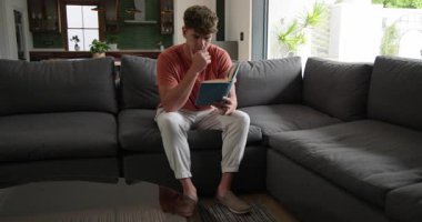 Açık mavi defterci adam, evdeki gri koltukta sayfaları çevirip pasajları okuduktan sonra. Gündelik, tefekkür, ev içi, yaşam tarzı, rahatlama, modern, rahat