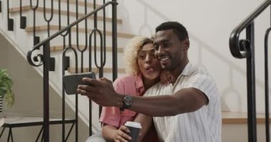 Karışık arkadaşlar birlikte gülerken akıllı telefona bakıyorlar, evde kahvenin tadını çıkarıyorlar. çeşitlilik, arkadaşlık, sohbet, teknoloji, sosyalleşme, yaşam tarzı