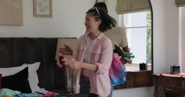 Çeşitli çiftler, yatakta uzanan, güneş gözlüğü takan ve seyahat için bavul hazırlayan kadınları selamlıyor. Gündelik, yaşam tarzı, modern, samimi, canlı, neşeli, düzenli.