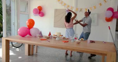 Farklı çiftler evde pasta ve şapkalarla kapalı bir doğum günü odasında parti yemeği ve dekor hazırlıyorlar. Kutlama, şenlik, toplanma, hazırlık, dekorasyon, atıştırmalıklar, balonlar, canlı