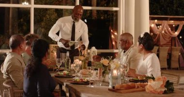 Çeşitli gruplar için şarap dolduran bir adam bahçede düğün kutlaması yapıyor. Konukseverlik, yemek, hizmet, toplanma, keyif