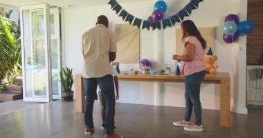 Çeşitli aileler evde doğum günü kutluyor, balonlarla ve parti şapkalarıyla süslüyor. Kutlama, farklı aile zamanları, doğum günü partisi, dekorasyon, mutluluk, birliktelik.