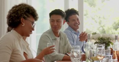 Çeşitli arkadaşlar şarap kadehlerini kaldırırken aynı zamanda bahçeye bakan ahşap masanın etrafında gülüyorlar. Kutlama, yoldaşlık, neşe, sosyalleşme, kırsal, hareketli, neşeli