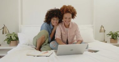 Çift cinsiyetli lezbiyen çift yatakta dizüstü bilgisayar kullanıyor, gülümsüyor ve evde tartışıyorlar. LGBTQ, teknoloji, iletişim, gündelik, bağlantı, ilişki