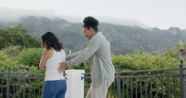 Afrikalı Amerikalı bir adam Asyalı Çinli bir kadını terasta döndürüyor, battaniyeli bir kupayla sürpriz yapıyor. Romantik, mahremiyet, açık hava, manzara, neşeli, hassas, kutlama