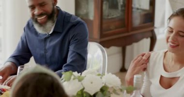 Yemek masasındaki misafirleri selamladıktan sonra Afro-Amerikan adam yemeği paylaşmak için kaseden salata servis ediyor. Aile, misafirperverlik, birliktelik, kutlama, doğal ışık, samimi, samimi