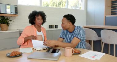 Afro-Amerikalı çift belgeleri inceliyor ve mutfak masasında tablet kullanıyorlar. İş, işbirliği, planlama, finans, teknoloji, takım çalışması