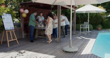 Arka bahçede kutlama yapıyorlar, farklı yaşlılar havuz kenarında sohbet ediyor ve içecekler içiyorlar. Boş zaman, rahatlama, kutlama, keyif, yaz