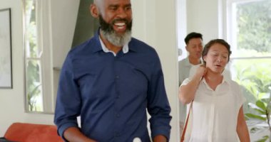 Sakallı Afro-Amerikan bir adam ailesine oturma odasında rehberlik ediyor, temiz bir şişe seçiyor ve gülümsüyor. Aile, çok nesilli, birliktelik, kutlama, bağlantı, modern, canlı