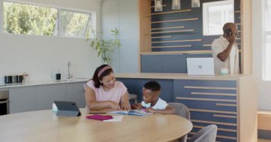 Değişik bir anne oğluna mutfak masasında ödevlerinde yardım ederken baba telefonda ve evde konuşuyor. çeşitli aile, eğitim, ebeveynlik, iletişim, takım çalışması, çoklu görev