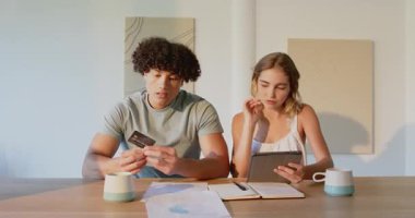 Evde tablet ve kredi kartıyla finans işleriyle uğraşan genç bir çift. Bütçe, teknoloji, para, harcama, çevrimiçi, yaşam tarzı