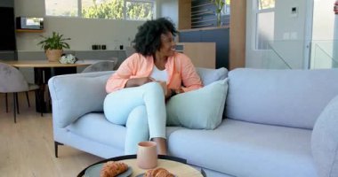 Genç çift evde kahvenin tadını çıkarıyor, gülümsüyor ve kanepede dinleniyorlar. Rahatlama, yaşam tarzı, birliktelik, bağlanma, evcil, rahat