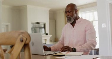 Pembe gömlekli son sınıf öğrencisi evde dizüstü bilgisayar ve not defteri kullanıyor, işine konsantre oluyor. Yaşlılar, teknoloji, çalışma alanı, ev ofisi, daktilo, üretkenlik