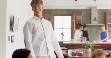 Oturma odasına giren bir adam, arkadaşları selamlıyor ve mutfak adasında içki dolduran önde gelen bir grup. Sosyal toplanma, misafirperverlik, çağdaşlık, rahatlama, kutlama, sıcaklık, neşe