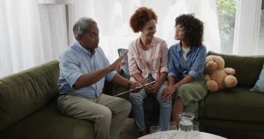 Yaşlı adam, evdeki kanepede aynı cinsiyetten gülümseyen lezbiyen çiftle fotoğraf albümünü paylaşıyor. lgbtq, bağ, aile, nostalji, mutluluk, birliktelik