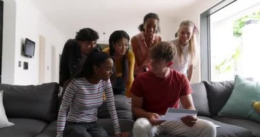 Çeşitli arkadaşlar sürpriz haberler için zarf açıp evdeki gri kanepede kutlama yapıyorlar. Arkadaşlık, kutlama, sevinç, sürprizler, sosyal toplanma, modern iç mekan, gündelik yaşam tarzı