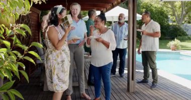 Arka bahçedeki kutlamaların tadını çıkaran çeşitli yaşlılar güneşli terasta gülüp sosyalleşiyorlar. Yaşlılar, mutluluk, çeşitli arkadaşlar, kahkahalar, toplanma, güneş ışığı