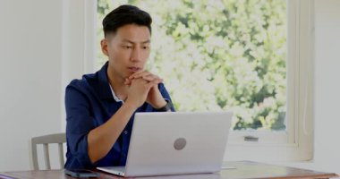 Masada dizüstü bilgisayarda yazan Asyalı adam, akıllı telefonu kontrol ediyor, kredi kartı ödemesini yapıyor, kutlama yapıyor. Uzak çalışma, teknoloji, kentsel yaşam tarzı, iş, konsantrasyon, üretkenlik, modern