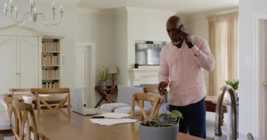 Evde dizüstü bilgisayarla çalışan Afro-Amerikalı bir adam telefonda konuşuyor. İş, iletişim, uzaktan çalışma, teknoloji, ev ofisi, çoklu görev