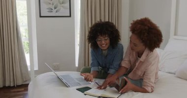 Çift cinsiyetli lezbiyen çift evde yatakta otururken dizüstü bilgisayarda mutlu bir şekilde sohbet ediyorlar. LGBTQ, teknoloji, iletişim, ilişki, konfor, bağlantı