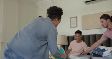 Tablet üzerindeki kontrol listesi, yatak odasındaki bavulları seyahat için hazırlayan çeşitli erkek arkadaşlar. Bagaj, seyahat, organizasyon, takım çalışması, günlük, canlı, hazırlık